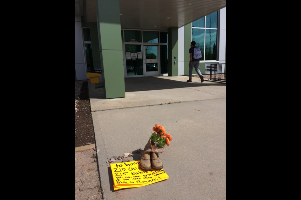 A pair of worn boots, a pile of stones and flowers were left outside the main entrance to the Lac La Biche Provincial Building on Tuesday morning with a sign recognizing the 215 children believed to have been recently found in unmarked graves at a BC residential school. The Lac La Biche Provincial Building houses Alberta government offices for 