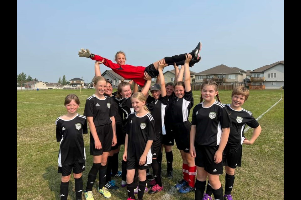 Bonnyville's U11 girls hoist up their goalie in celebration.