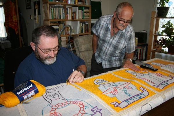 Father G érard Gauthier works on his latest tapestry at his home in St. Paul, which depicts the women of the Bible, while local artist Herman Poulin looks on.