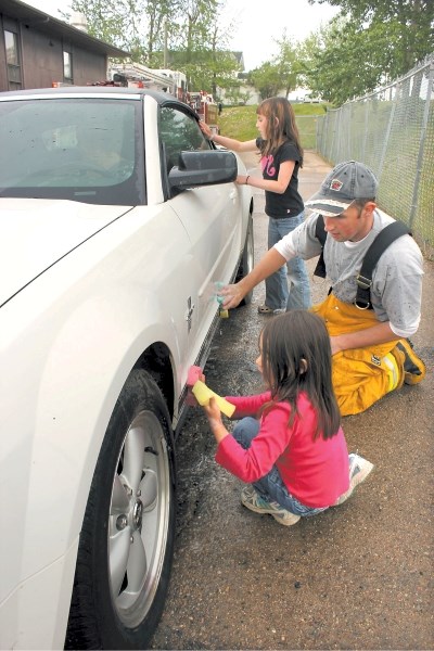 Lac La Biche firefighter Chris Newhook gets some help washing cars from his two daughters, Emily and Gwen, at last week&#8217;s car wash and barbecue fundraiser for Slave