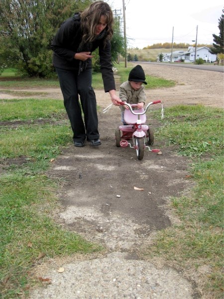 Tracy Lord and her son Helix, two, navigate a bumpy section of sidewalk in the Hamlet of Plamondon.