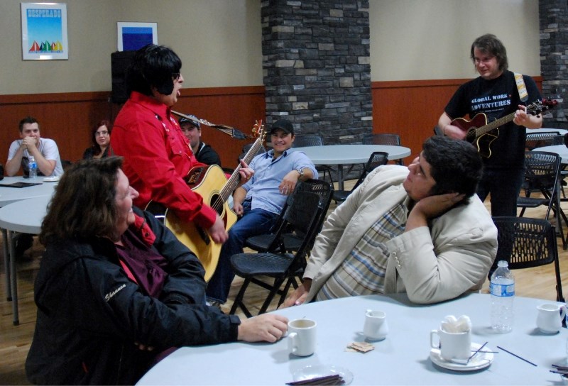 Mark Courtnage entertains the crowd as Elvis Presley with the accompaniment of Gerrit Kirchberg on guitar. Michael Wheeler enjoys being sung to as onlookers enjoy a laugh.