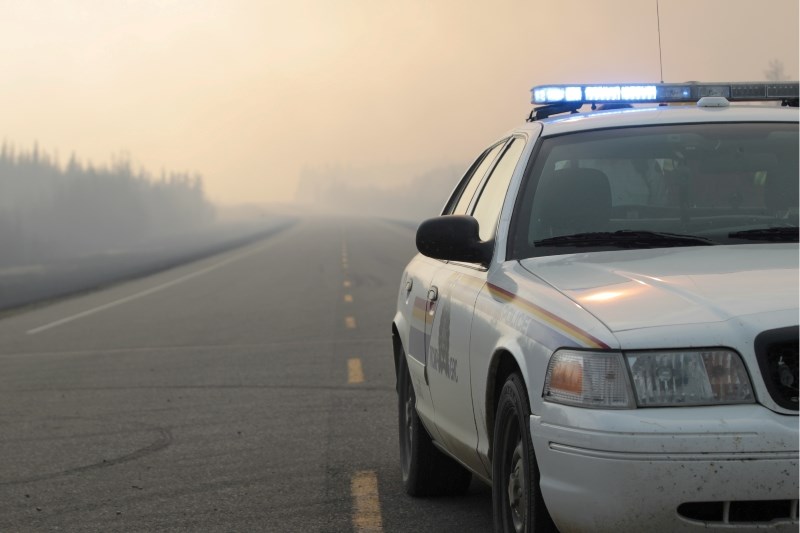 An RCMP cruiser blocks off the Alpac access road north of Wandering River on Sunday afternoon as an out-of-control wildfire throws up a smoky blockade behind. Officials