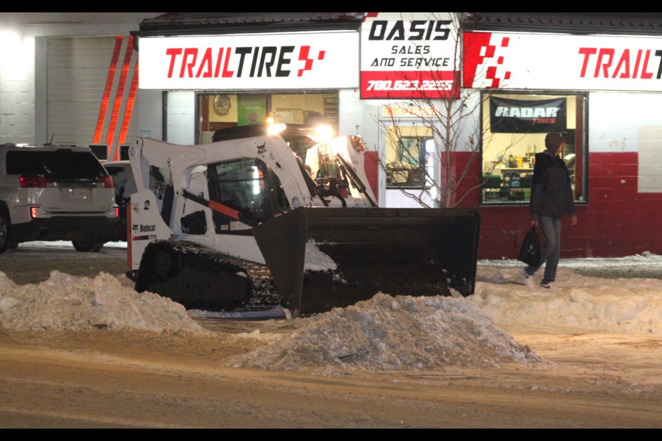 A pedestrian walks past a Bobcat machine that was clearing snow from the roadway and sidewalk areas of 102 Ave. (Main Street) in Lac La Biche. On Tuesday, Jan. 7, Lac La Biche County crews were out after 10 p.m. removing snow from streets in the downtown core of the hamlet of Lac La Biche. Chris McGarry photo. 