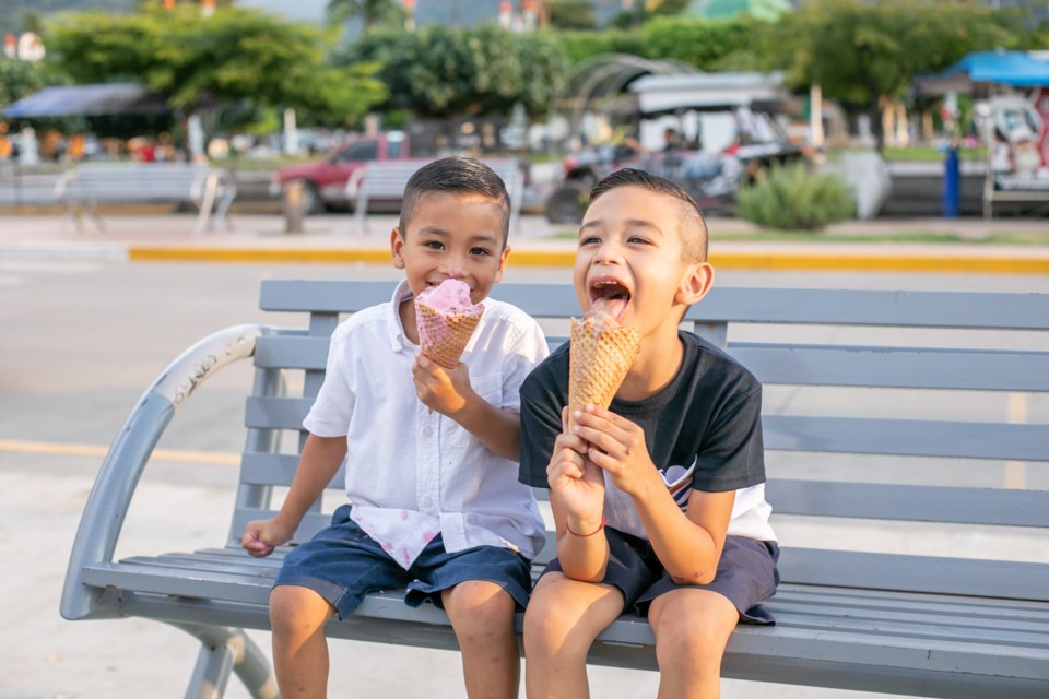 Two,Hispanic,Cheerful,Kids,Sitting,On,A,Bench,In,A