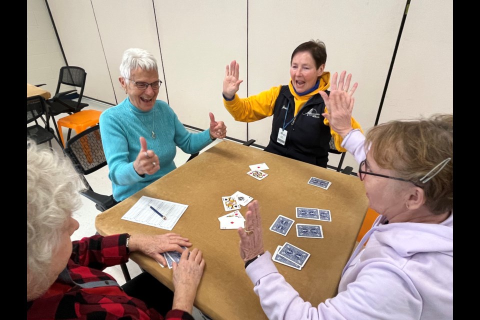 Gerry Peters and Jean Rutherford raise their hands in cheers as they celebrate whoever won the euchre game at their table.