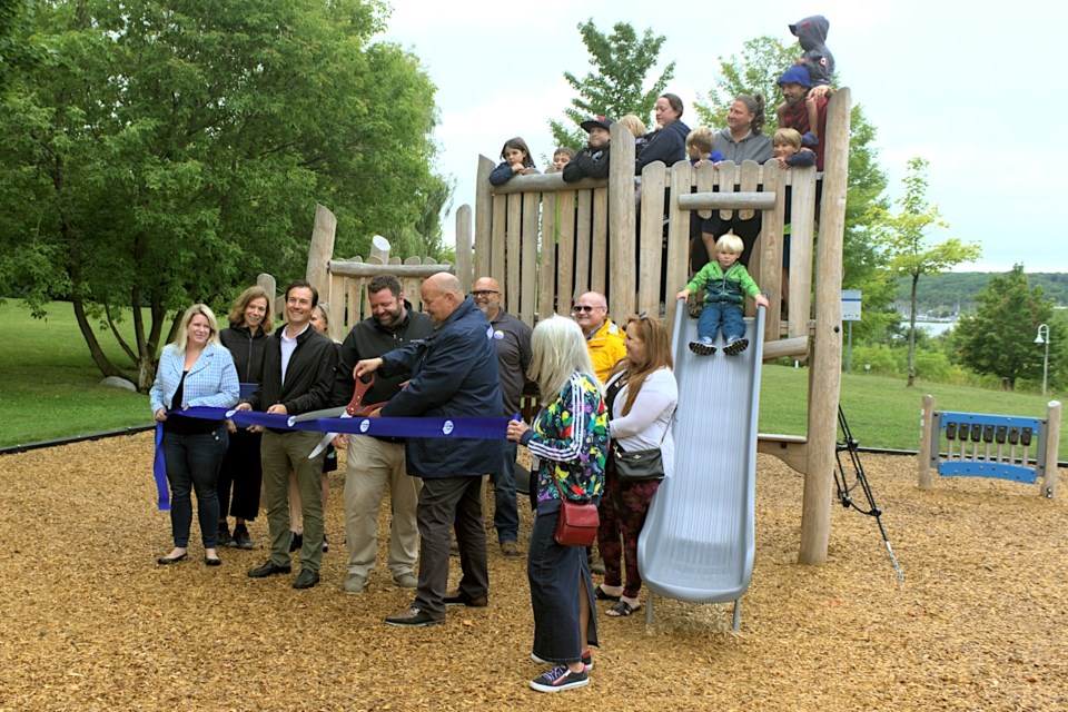 Midland Mayor Bill Gordon held the giant scissors to cut the ribbon on the Edgehill Park playground's reopening, surrounded by town staff, councillors, and local dignitaries. Rowan Everett, 3, sat on the slide with little interest in the formalities.