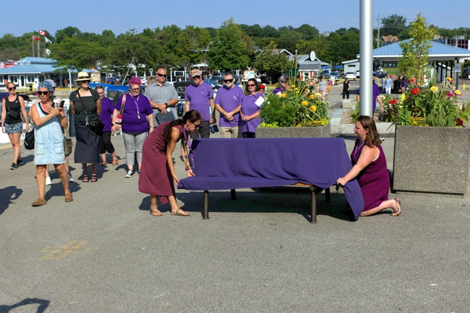 Haily MacDonald, acting executive director for Huronia Transition Homes (right), and Maison Rosewood Shelter crisis councillor Desiree Salis (left) placed a purple fabric over a harbour bench in Midland to signify the murder of Julia Brady and call for an end to intimate partner violence.