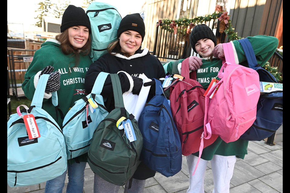 Student volunteers (from left) Maeve Conrad, Sienna Forsyth and Mariah Ferringo carry backpacks out to waiting cars for delivery as part of the annual Pack a Bag for a Friend campaign.