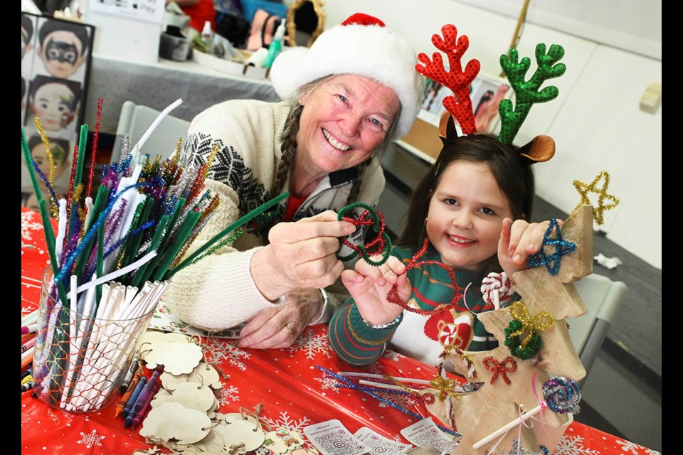 Seven-year-old Hope Souso Melo gets a helping hand from craft volunteer Gillian Burns as they make tree ornaments at the Santa at the Fairgrounds event.