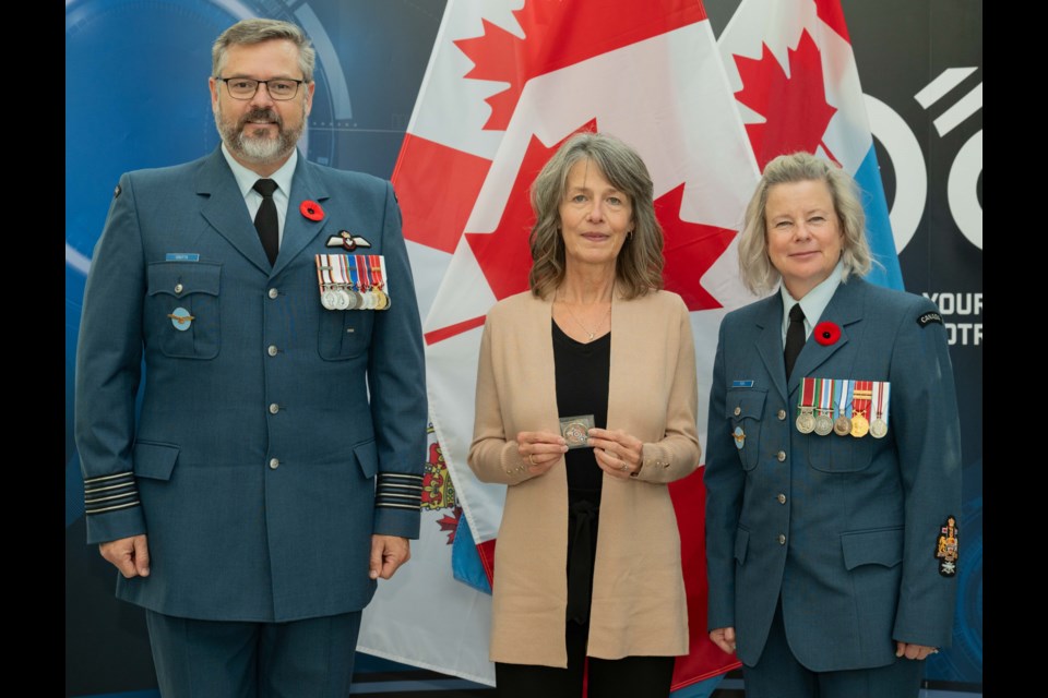 15 Wing Commander Col. Dan Coutts (left) and Chief Warrant Officer Rachel Fox present an RCAF 100 Coin to Donna Fritzke (centre). Photo by 15 Wing Imaging