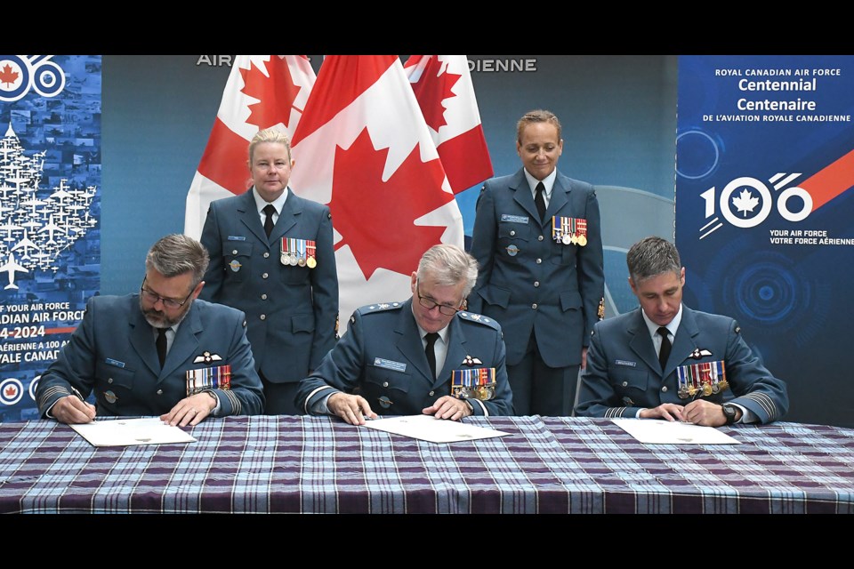 Incoming 15 Wing commander Col. Dan Coutts, reviewing officer Brig. Gen. J.J. Alexander, and outgoing 15 Wing commander Col. Jonathan Bouchard sign the change of command documents as Chief Warrant Officer Rachel Fox and Division Chief Warrant Officer Marlene Shillingford look on.