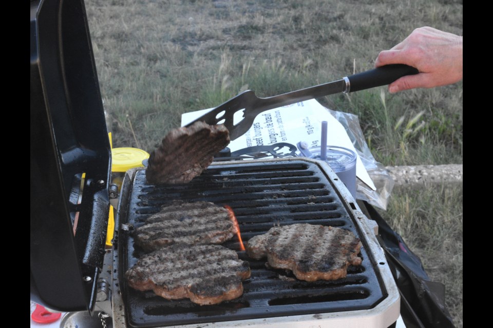 Burgers sizzle on a barbecue as volunteers prepare supper for less fortunate residents. Photo by Jason G. Antonio