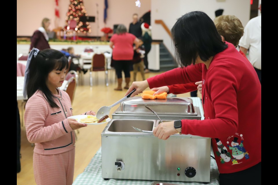 Betty Baril of the Kiwanis Club of Olds dishes out a sausage to Rylie Deleon, 7, during Breakfast With Santa.