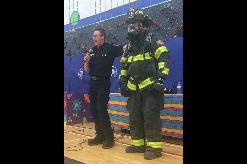 DON'T BE INTIMIDATED – With some help from Lt. Scott Parker, right, Capt. Ryan Martens of the Sundre Fire Department demonstrates to River Valley School students on Oct. 12 the kit worn by a firefighter who’s preparing to enter a structure fire to search for anyone who’s trapped or needs help. Students in kindergarten to Grade 6 were told if they ever find themselves in such a situation not to hide from or be scared by what can in the chaotic conditions created by a fire appear to be quite an intimidating presence who sounds – and in thick smoke with the helmet on might even look – like Darth Vader. 
Simon Ducatel/MVP Staff