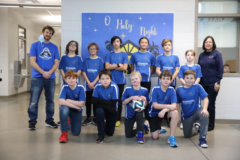 Holy Trinity Catholic School soccer players show off the uniforms they received, thanks to a $1,500 donation from the Kiwanis Club of Olds. On the far left, is coach and teacher Kyle Young. On the far right is Kiwanis Club of Olds president Betty Baril.