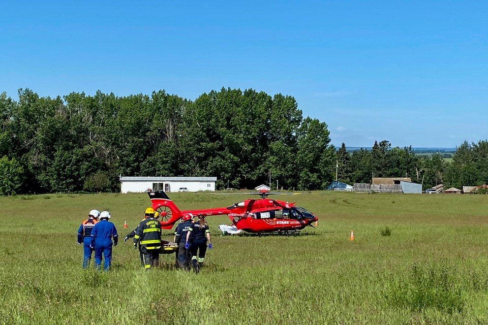 Innisfail firefighters help load the seriously injured woman into a waiting STARS air ambulance after a single-vehicle rollover northeast of Innisfail on the morning of June 22. Submitted photo