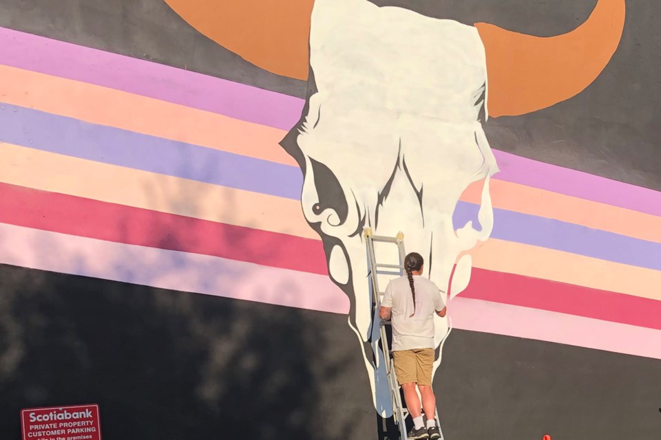 Artist Ryan Willert works on the buffalo skull image on the side of the Century Theatre in Innisfail.