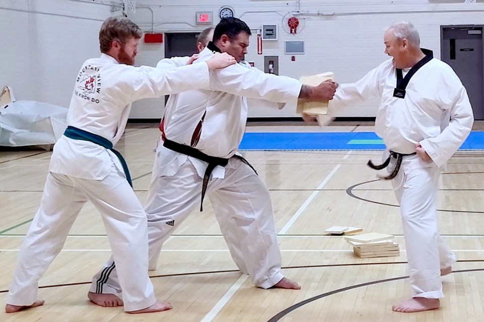 Jim Hall, a longtime member of the Mountainview Taekwondo Club who was recently testing for his second degree black belt, punches through a wooden board held up by Wade Johnson with some support from Neill O’Rodaigh. Submitted photo