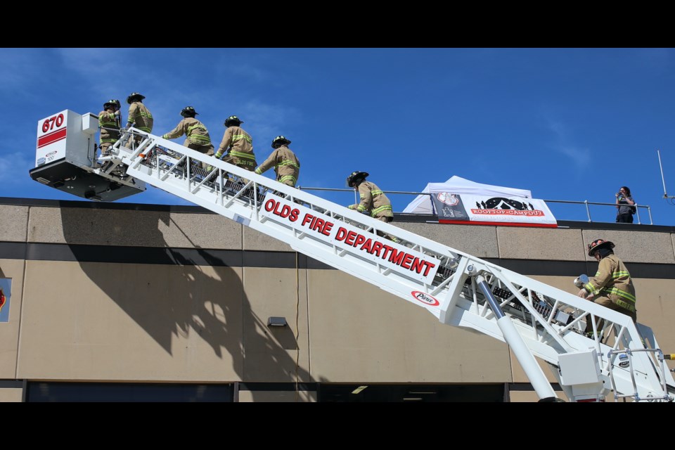 At 12 noon sharp on Friday, firefighters ascend to the roof via an Olds fire department ladder truck. Doug Collie/MVP Staff