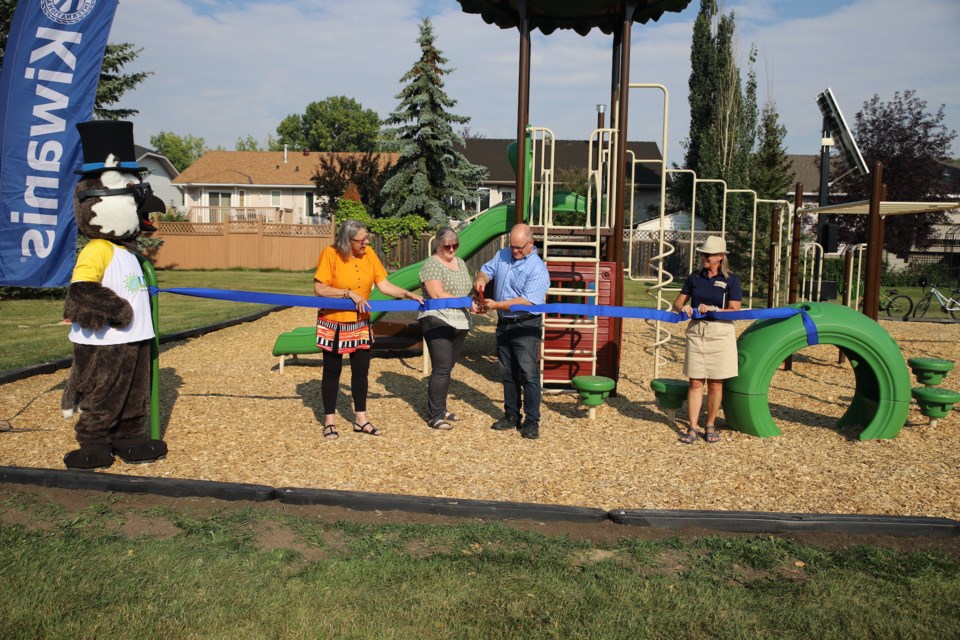 Town mascot Oliver Olds (who must have been extremely hot in the heat that day) looks on as, from left: Town of Olds Mayor Judy Dahl, Jean Statham’s daughter Elaine Brandenburg and son Lyle Statham, and incoming Kiwanis Club of Olds president Annelise Doolaege combine to cut the ribbon officially opening the Kiwanis Jean Statham Playground. 