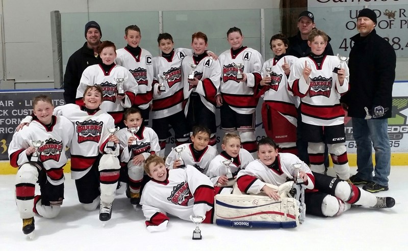 The Sundre peewee A Huskies triumphantly hold up their trophies in celebration of winning the team&#8217;s home tournament, which was held Dec. 9-11.,