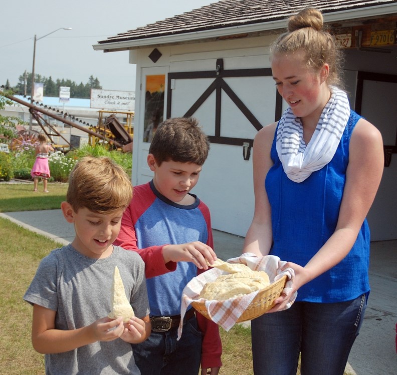 Kayleigh Wolfe, summer student and assistant manager at the Sundre Pioneer Museum, serves up some fresh baked bannock bread to friends Gavin Battrick, left, and Logan Voisey