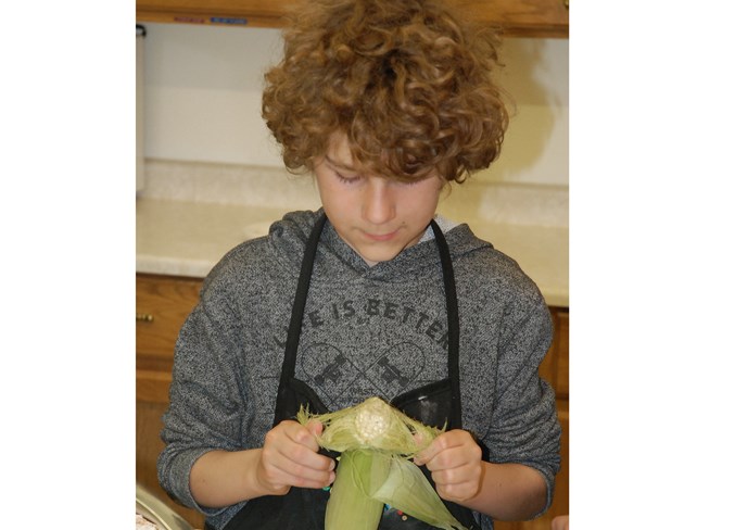  Zander McNutt husks some corn on the cob.