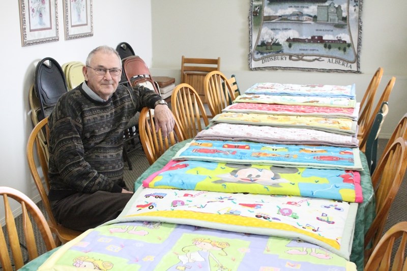 Lorne Halbauer sits beside some quilts.