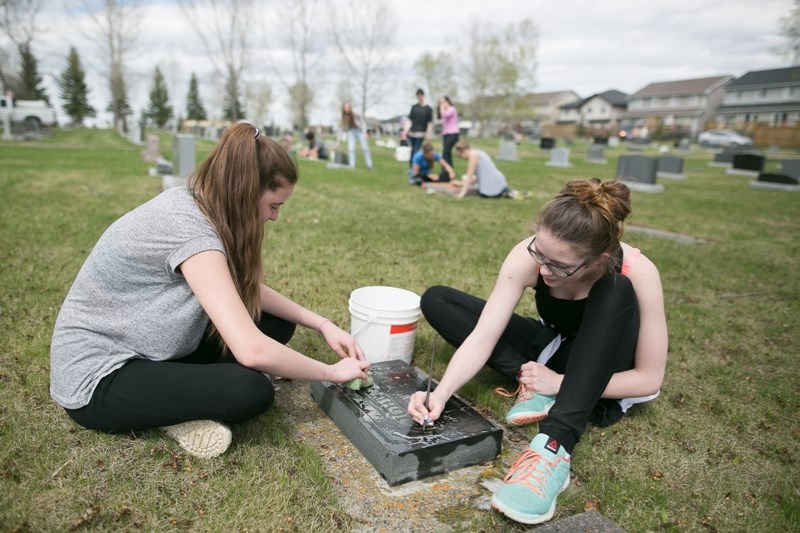 Didsbury High School Grade 12 students Kallie Hickling, left, and Hanna Van Besouw clean a headstone at the Didsbury Cemetary as part of the May Monarch program.