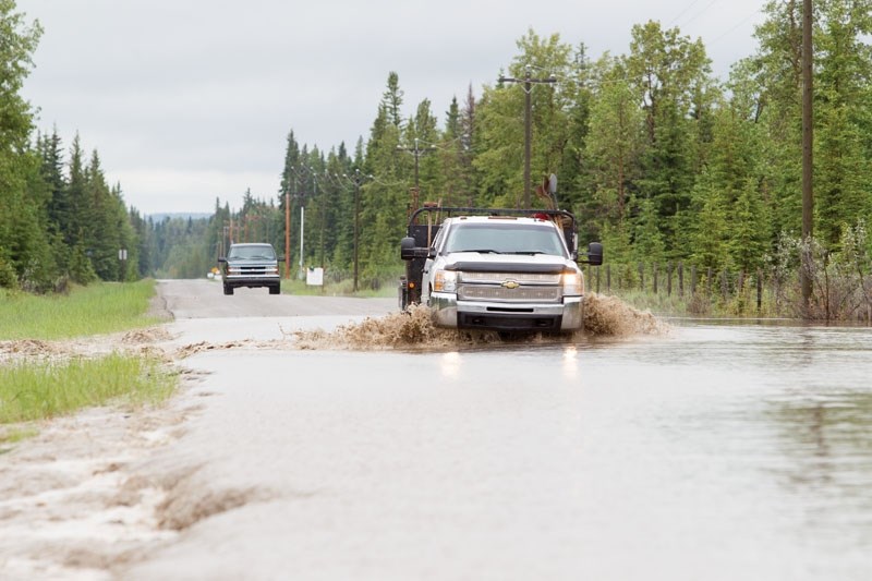 Trucks make their way across a flooded roadway west of Sundre.