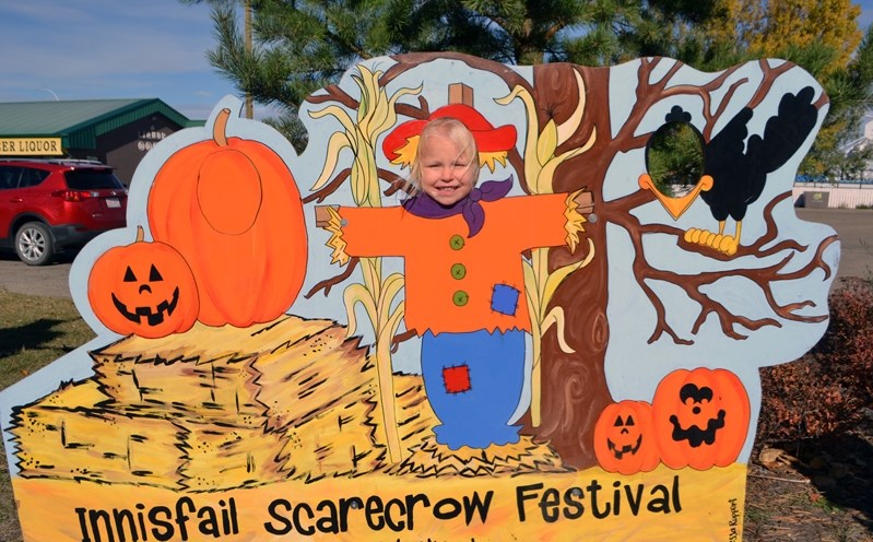 Ameliya McNichols, 3, of Blackfalds. pokes her head through the hole in the Scarecrow Festival sign that was set up on Main Street.