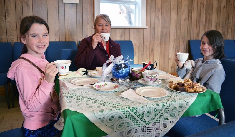 Izabelle Arsenault, left, and her twin sister, Elizabeth, join their step-grandmother Judy Serl for some tea and goodies during the Christmas Tea at St. Mark&#8217;s Anglican 