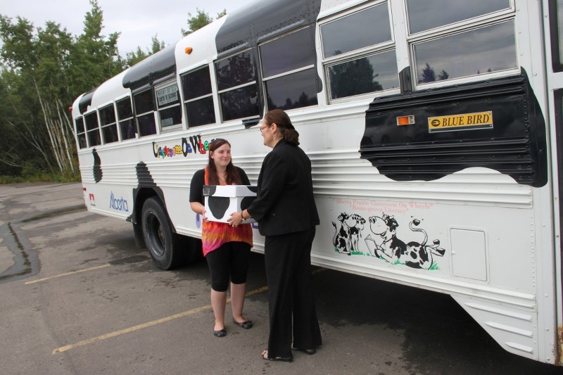 Amanda Di Marco, from Classroom On Wheels (COW), hands library manager Laurie Hodges a box filled with 50 donated books for the Innisfail Library. The books were donated by