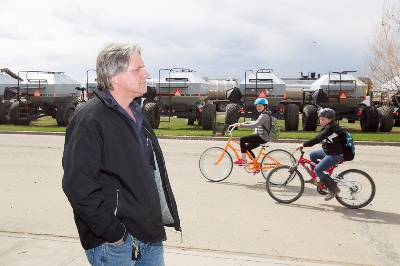 Penhold School students make their way home after school as Kevin Small looks on across the street from a planned expansion of Custom Bulk Services in Penhold on May 8.