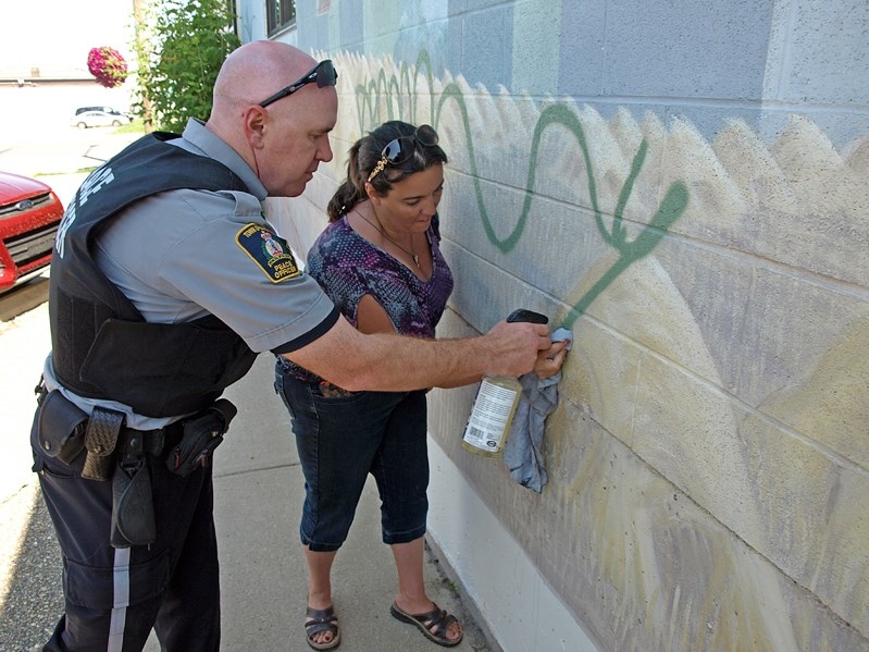 Innisfail community peace officer Ryan Anderson and Tammy Oliver-McCurdie, manager of the town&#8217;s FCSS office, attempt to remove graffiti from a downtown mural with a