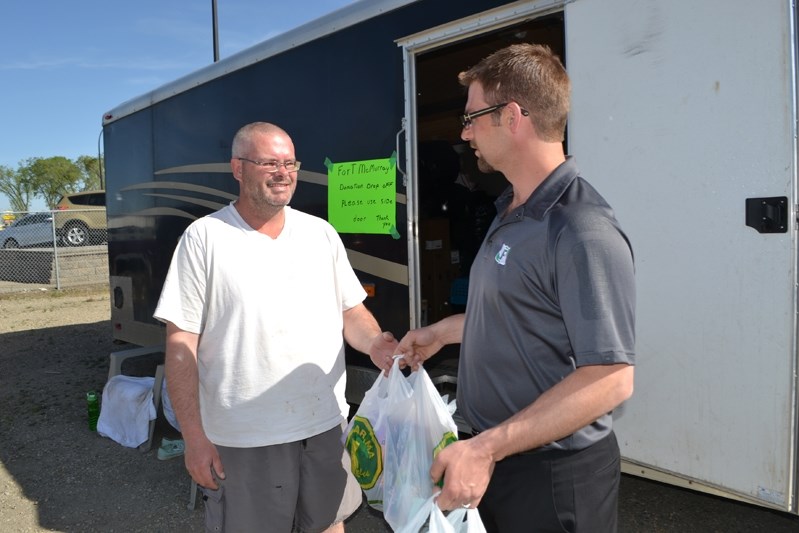 Jeffrey Verhaeghe, sales manager at FourLane Ford (right), hands Andy Laing bags of donated supplies for the displaced citizens of Fort McMurray. The Innisfail car dealership 