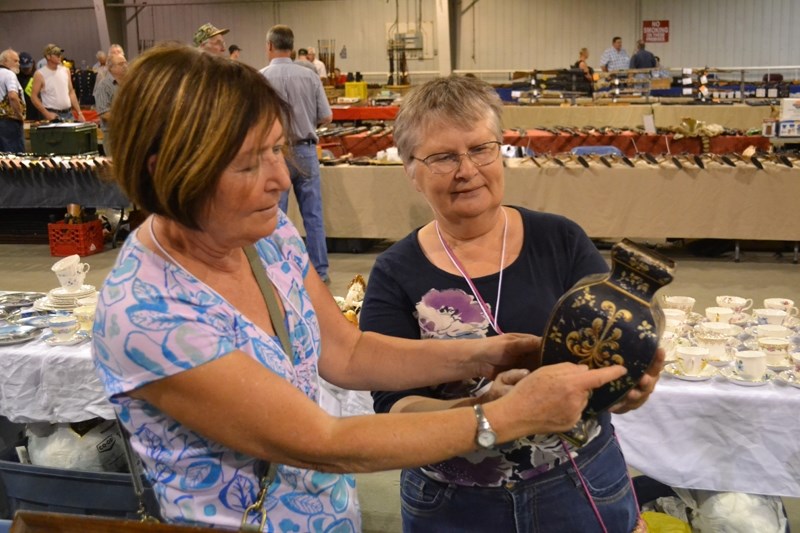 Janice Yeats and Andrea Ware examine an old tin vase for sale in their booth at the Olds Gun and Antique Show.