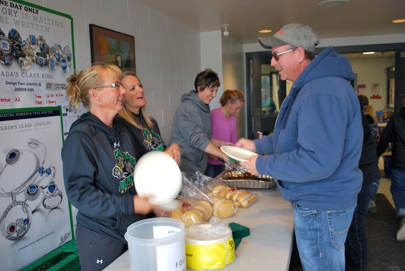 Tara Rankin, Shannon Belton, Kim Rude and Sydney Sparks serve burgers and hot dogs as Don Rude steps in line at the community barbecue held at Bowden Grandview School