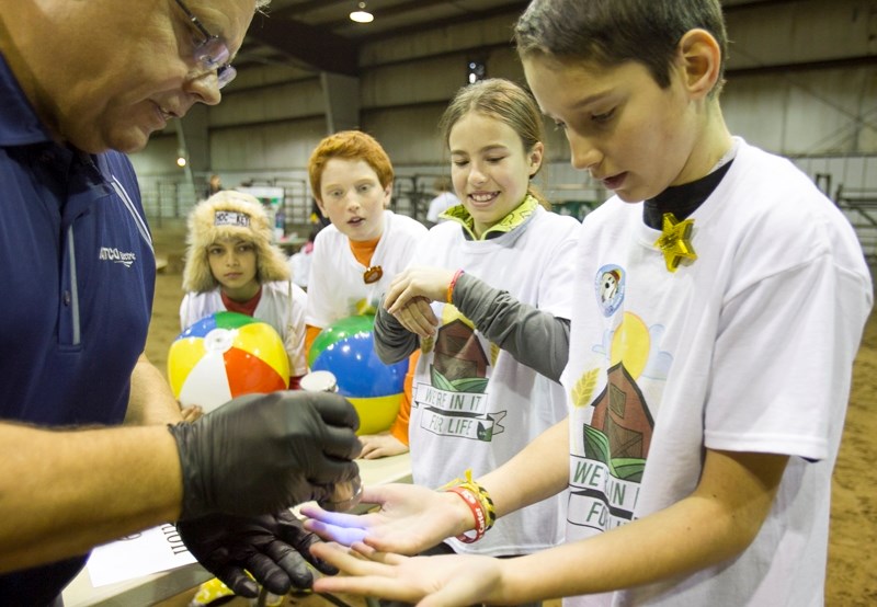 Grant Hoff, left, shows Ecole Deer Meadow School Grade 6 student Peyton Lobe germs on his hands with a black light during a agricultural safety event at the Caluori Pavilion