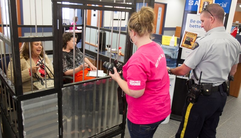 Tami Gardner, left, and Kathy Kimpton are &#8220;locked&#8221; into a jail cell by ATB Financial employee Taya Haarstad during a Jail-N-Bail fundraiser at the ATB branch in