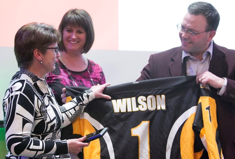 Mary Wilson receives a Grizzlys jersey from Doug Wagstaff as special recognition for her contributions to girls hockey in Olds during a banquet for the Midget Female A