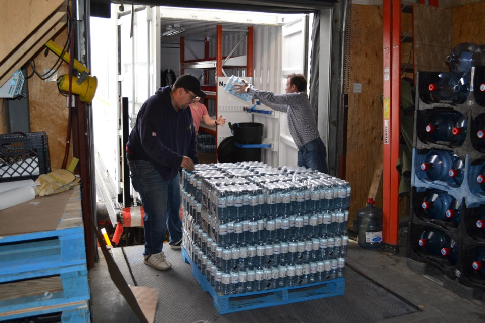 Tara Oilfield Services owner Martin Sheridan tosses a pack of water bottles into a company seacan at Peter&#8217;s No Frills in Olds while an employee gets ready to toss