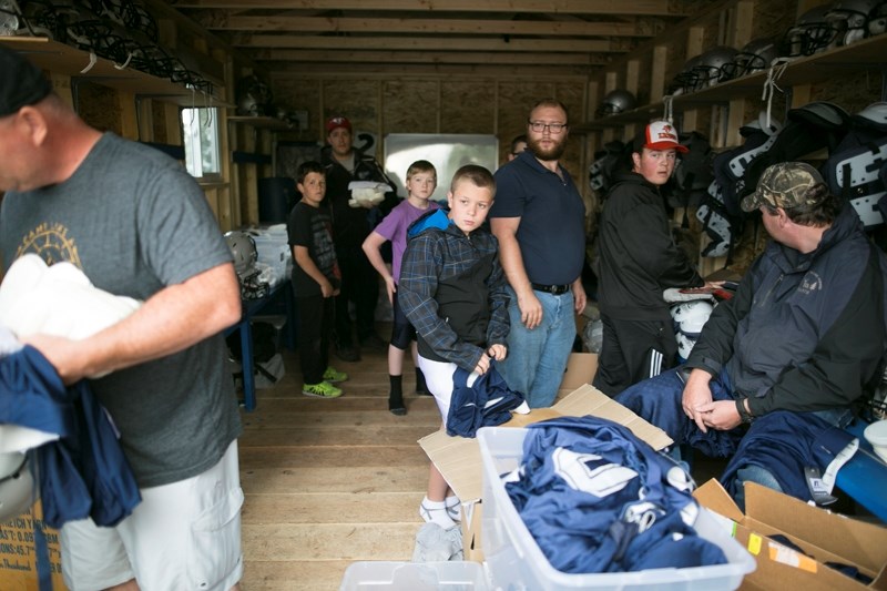 Olds Minor Football Huskies player Colin Black, middle, tries on football pants during a football equipment sign-out in an equipment building behind Olds High School on Aug.