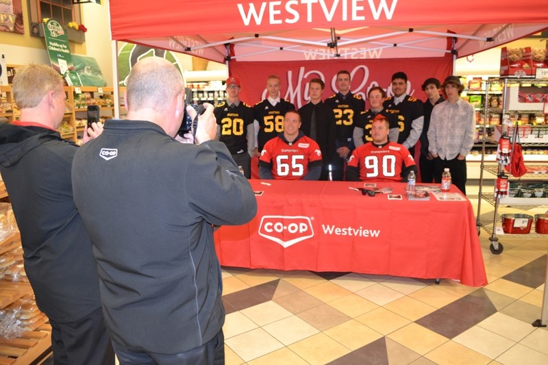 Co-op staff members take pictures as Calgary Stampeders Dan Federkeil and Quinn Smith pose for a photo with members of the Olds High School Spartans football team. Smith and