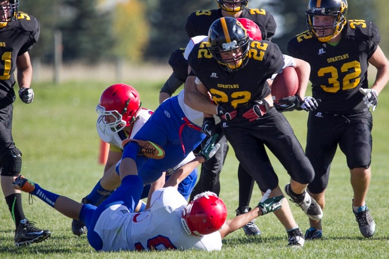 A Spartans player gets tackled by a pair of Bulldogs players.