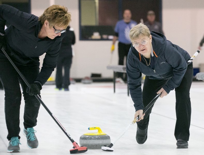 Brenda Turville, left, and Ruth Lind sweep a rock during the Olds Farmerettes Bonspiel at the Olds Curling Club.