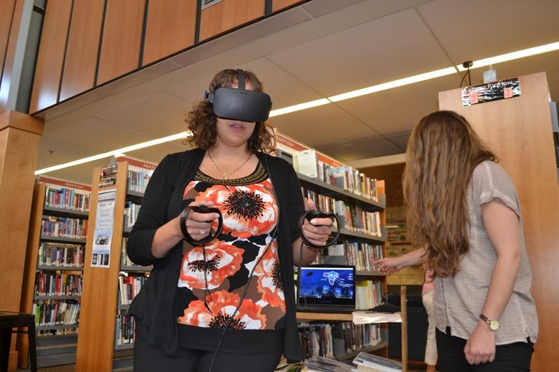 Rawan Kemaldean, left, tries swimming in the ocean via virtual reality, while her sister, Ceima Kemaldean, a computer coordinator at the Olds Municipal Library, shows what