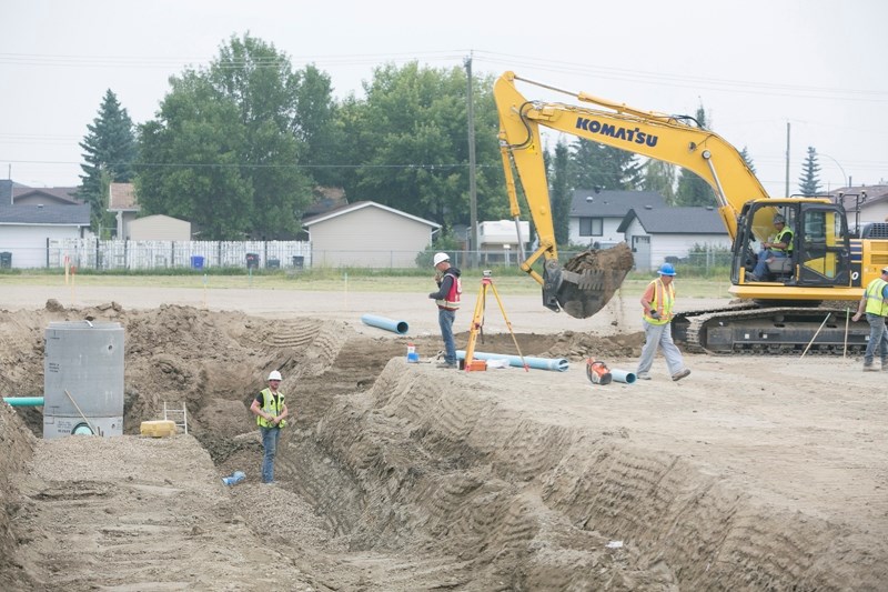 A construction crew trenches in sewer and water services for a new residential/commercial area in the former Olds High School track field, just north of Grouchy Daddy&#8217;s.