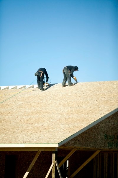 Two construction workers apply oriented strand board to the roof of a house off of 57 Avenue last Tuesday.